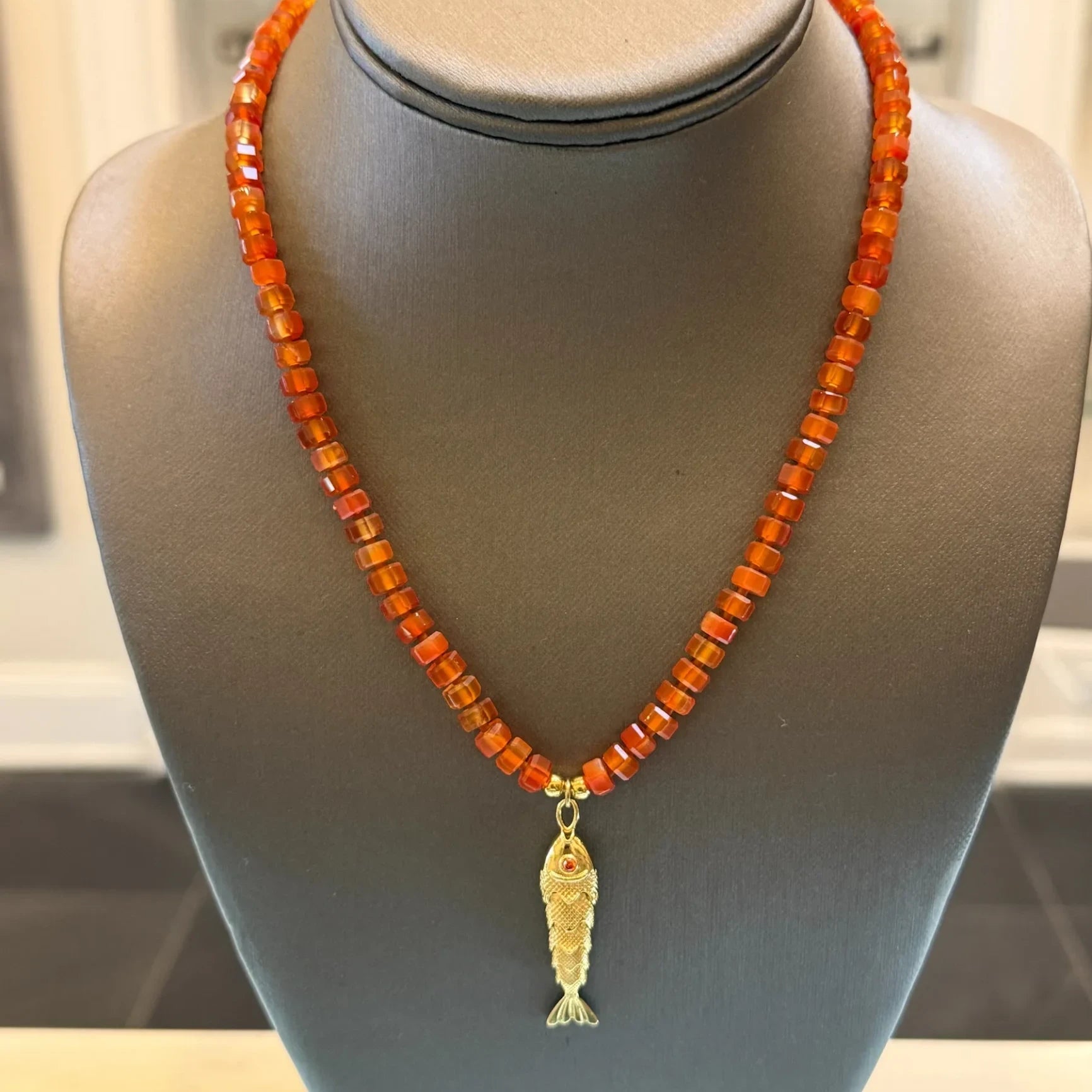 CHAKARR beaded necklace featuring amber-hued faceted gemstone beads and a gold-tone fish pendant on a display bust.