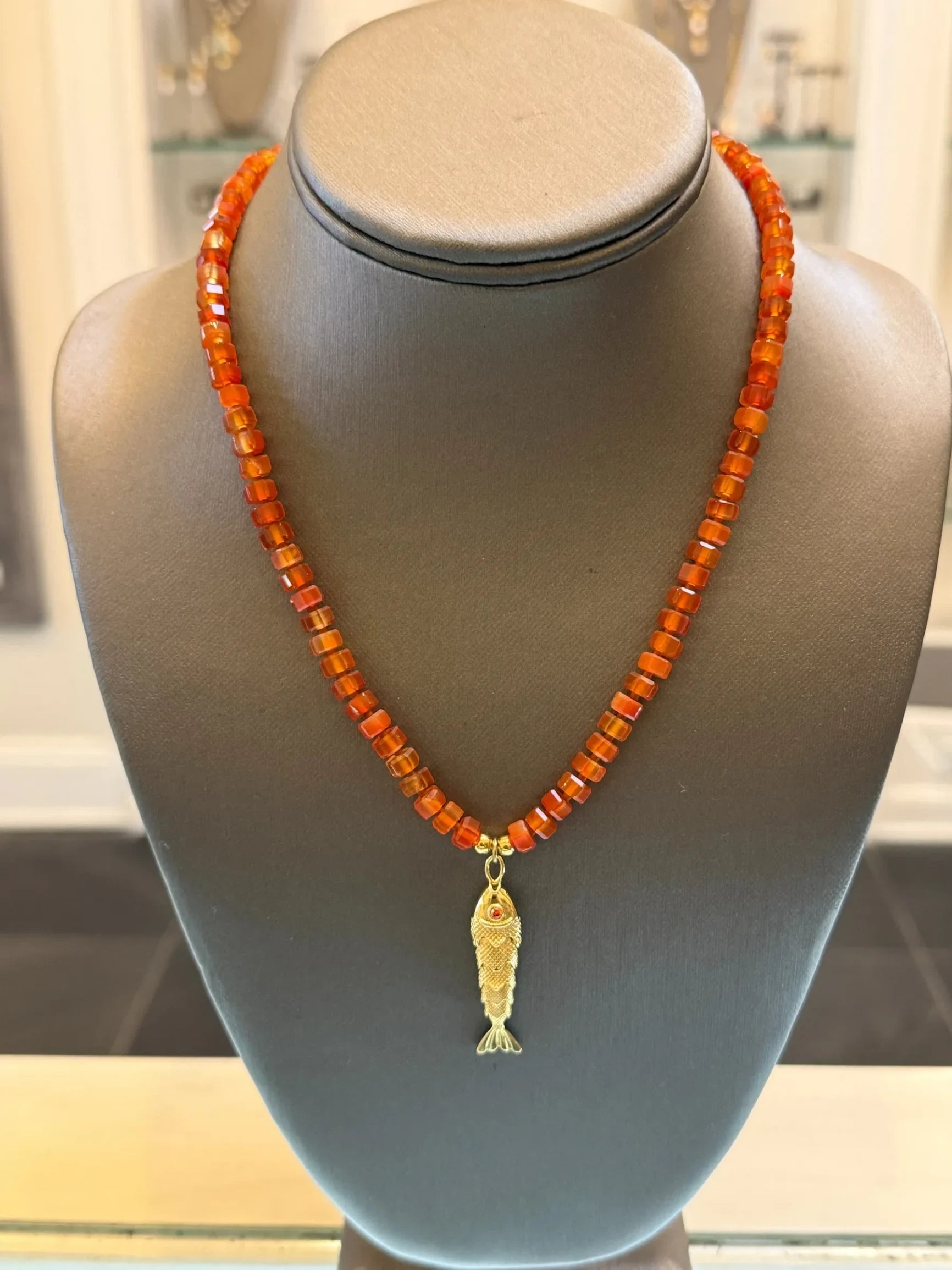 CHAKARR beaded necklace featuring amber-hued faceted gemstone beads and a gold-tone fish pendant on a display bust.